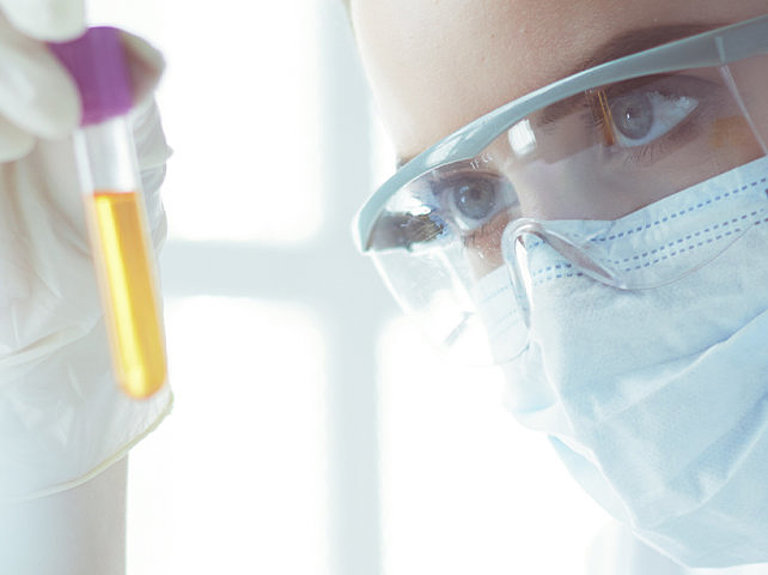 Frau mit Mundschutz untersucht Probe im Reagenzglas