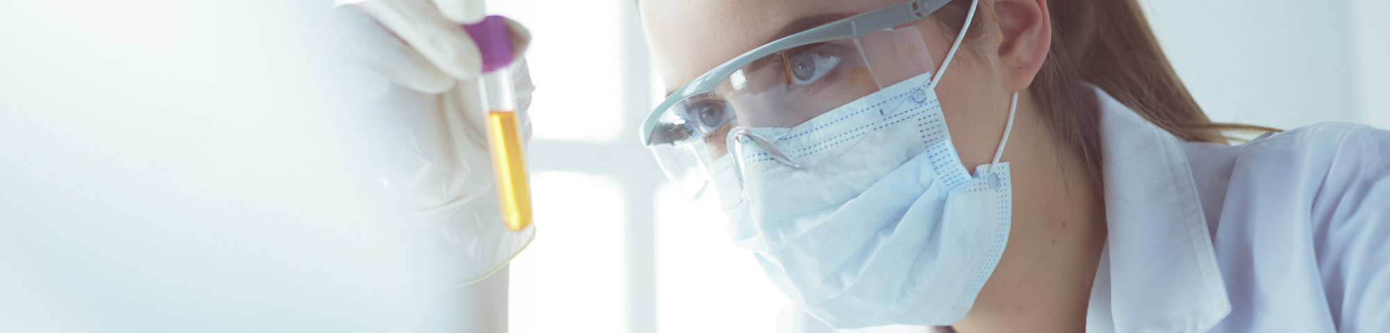 Frau mit Mundschutz untersucht Probe im Reagenzglas