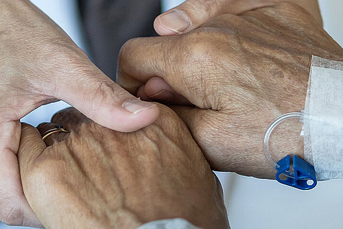 Seniorin auf der Palliativstation im Krankenhaus hält Hand einer Pflegerin
